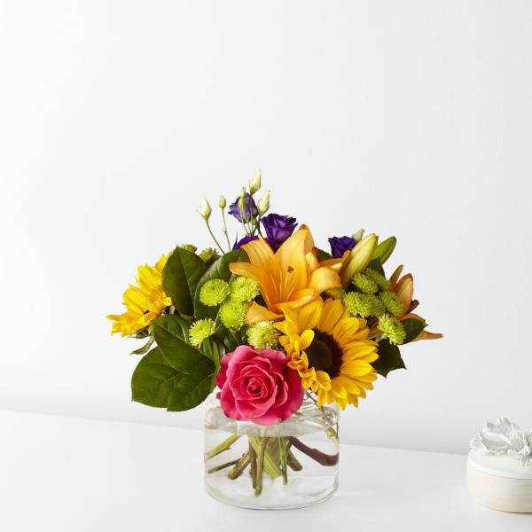 Mixed bouquet in a clear glass vase with a pink rose and yellow flowers