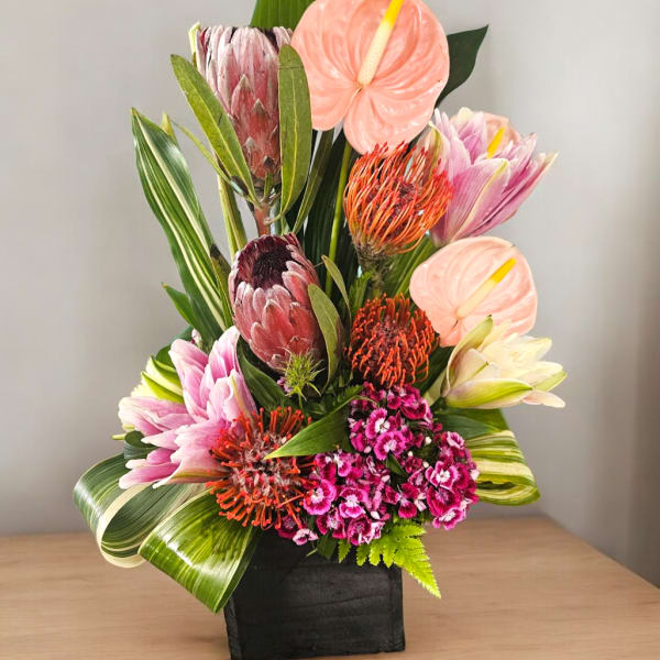 Tropical flower arrangement in a black container with pink and orange blooms