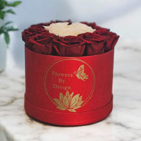 Red roses arranged in a round red box with a white rose center