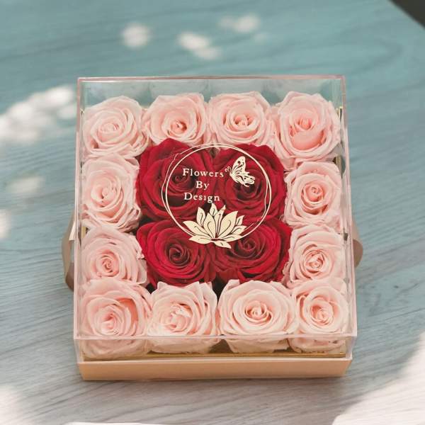 Boxed arrangement of pink and red roses in a clear square container