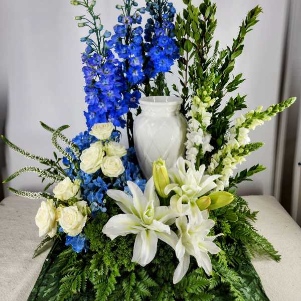 White lilies and roses with blue delphinium in a white vase