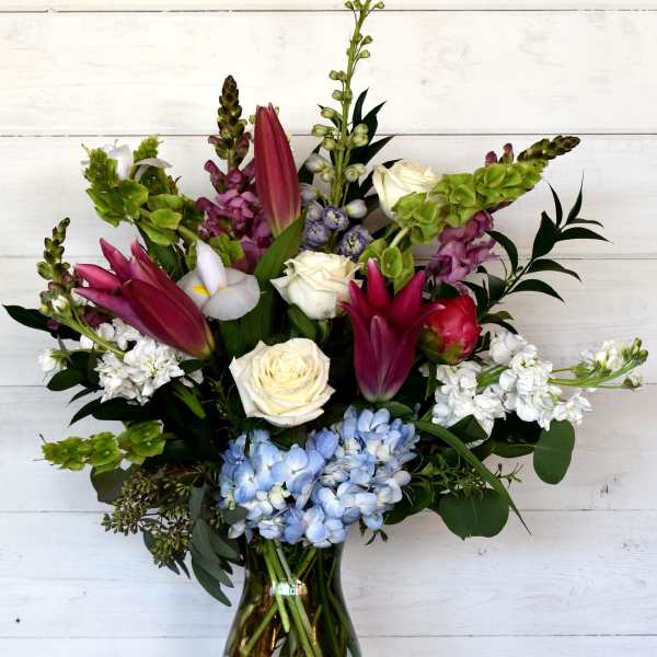 Mixed bouquet in a glass vase with pink lilies, white roses, and blue hydrangeas