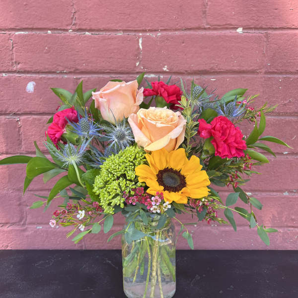 Mixed bouquet with roses, sunflower, and pink carnations in a glass vase