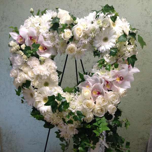 Heart-shaped white floral wreath on a stand with trailing ivy