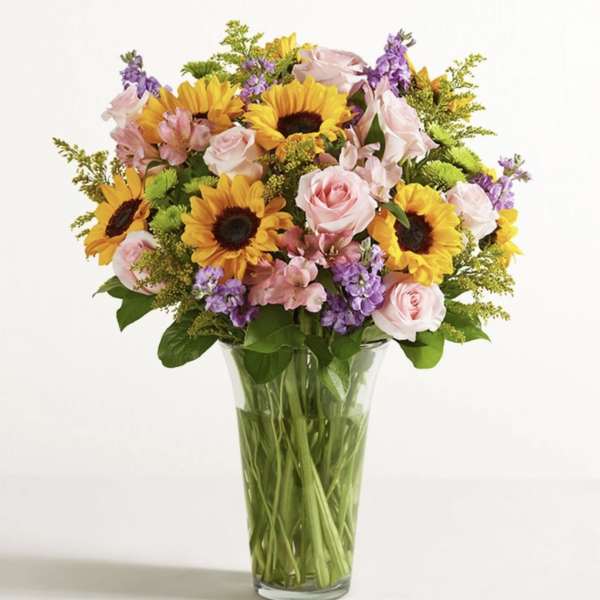 Bouquet of sunflowers, pink roses, and purple flowers in a glass vase