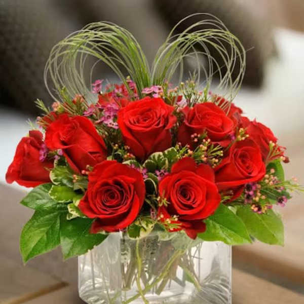 Red roses arranged in a clear square glass vase with decorative loops