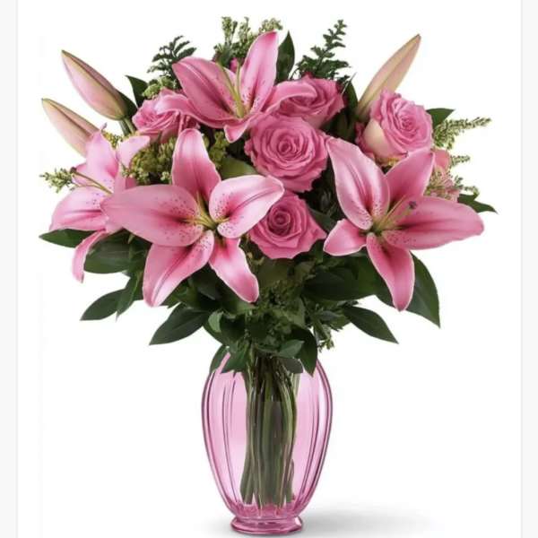 Pink lilies and roses arranged in a pink glass vase