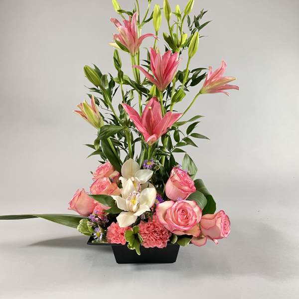 Tall floral arrangement with pink lilies, roses, and white orchids in a black vase