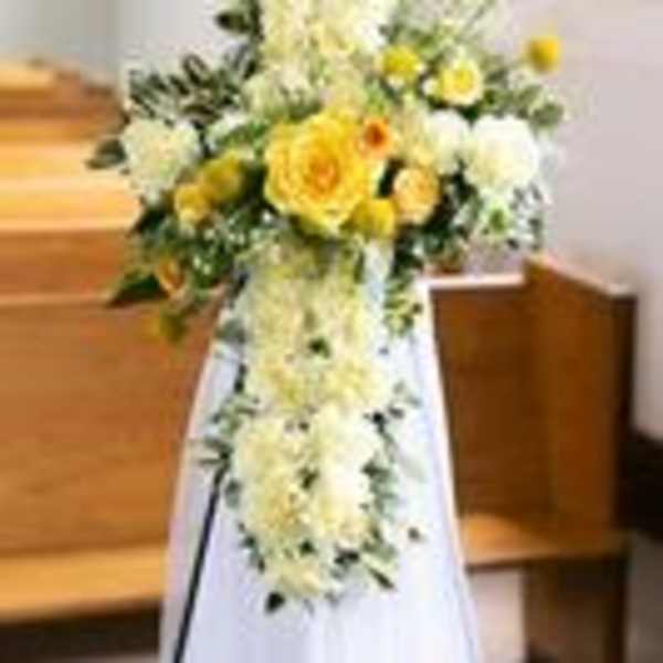 Standing cross-shaped arrangement of white and yellow flowers on an easel in a church aisle