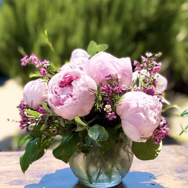 Pink peonies arranged in a glass vase with small purple filler flowers