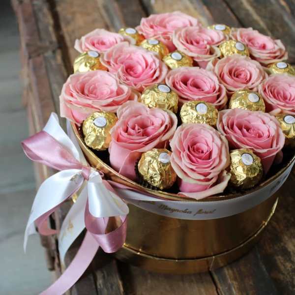 Pink roses and gold-wrapped chocolates in a round box with a ribbon bow