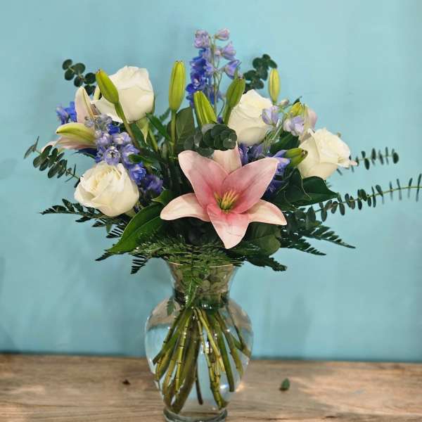 Pink lily and white roses in a glass vase with blue flowers