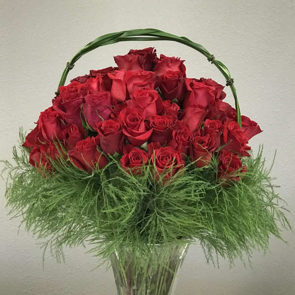 Red roses arranged in a clear glass vase with a green handle
