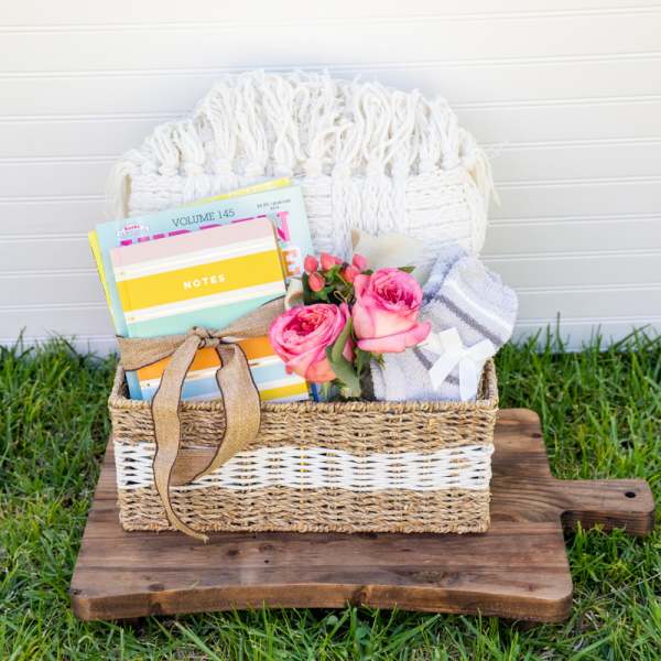 Gift basket with pink roses, a notebook, and folded blanket