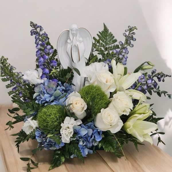 White angel figurine surrounded by blue and white flowers in a low arrangement