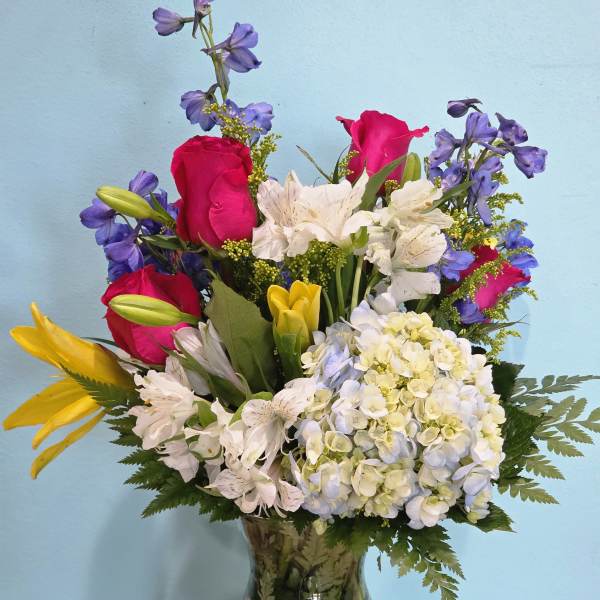 Mixed bouquet of roses, lilies, hydrangea, and blue flowers in a glass vase