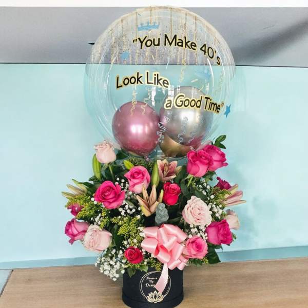 Pink rose arrangement with a clear balloon and metallic balloons in a black box