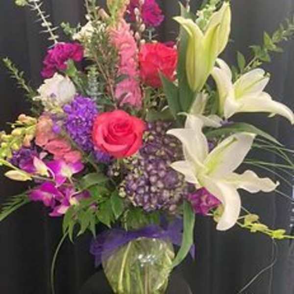 Mixed bouquet with roses, lilies, and purple flowers in a glass vase