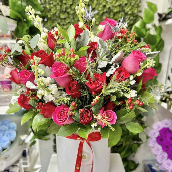 Large arrangement of red and hot pink roses in a white hatbox-style container with mixed filler flowers