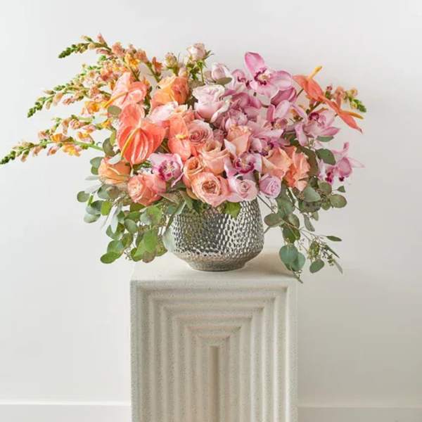 Pink and peach floral arrangement in a textured silver vase