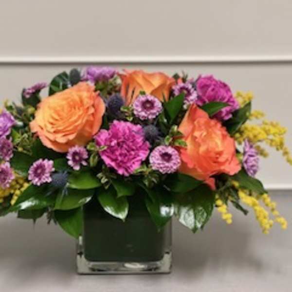 Orange roses and purple flowers in a square glass vase