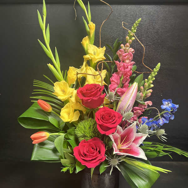 Mixed bouquet with red roses, yellow lilies, and pink blooms in a dark vase