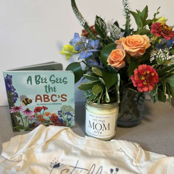 Flower arrangement beside a children’s book, candle, and baby onesie