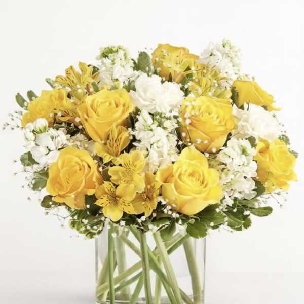Yellow roses and white flowers arranged in a clear glass vase