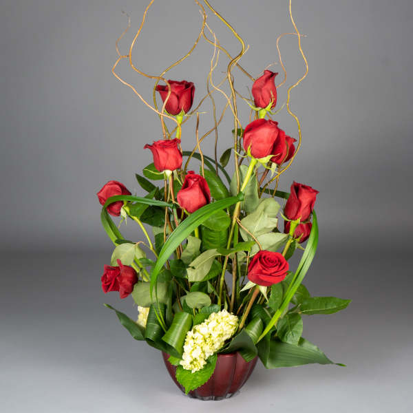 Tall arrangement of red roses in a burgundy vase with curly branches