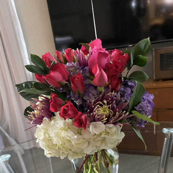 Bouquet of pink roses, purple blooms, and white hydrangeas in a glass vase