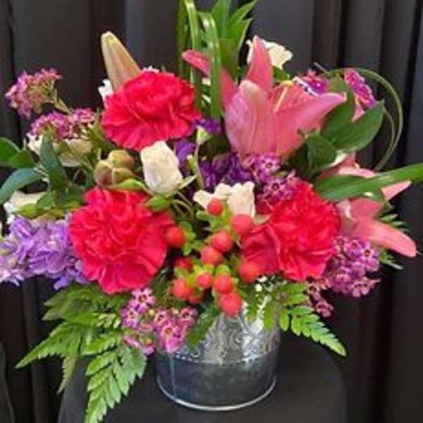 Mixed bouquet of pink lilies, carnations, and purple flowers in a metal vase