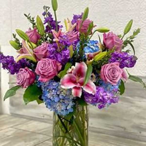Bouquet of pink roses, purple flowers, and blue hydrangeas in a glass vase