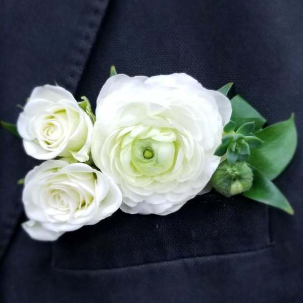White floral boutonniere pinned to a dark suit jacket