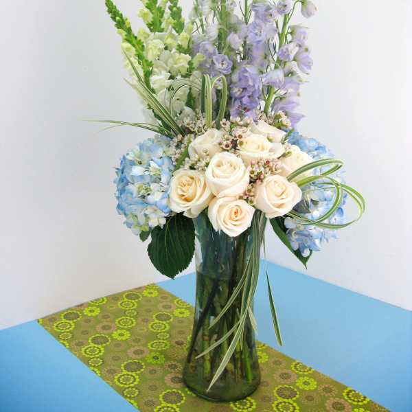 Blue hydrangeas and cream roses in a tall glass vase with lavender spikes