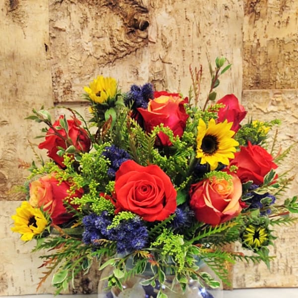 Mixed bouquet of red roses and yellow sunflowers in a round glass vase