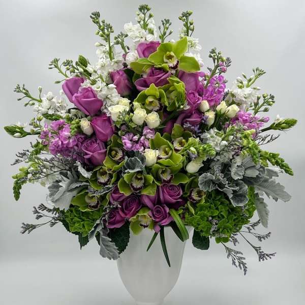 Purple roses and green orchids in a white vase
