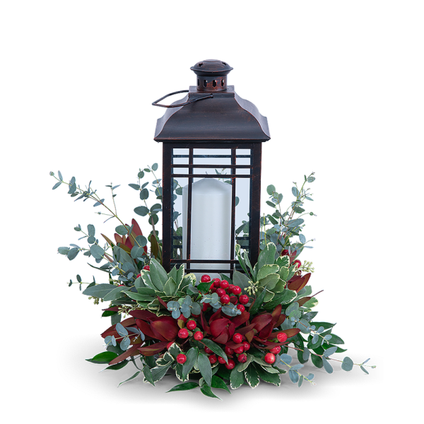Black lantern with a white candle surrounded by red berries and greenery