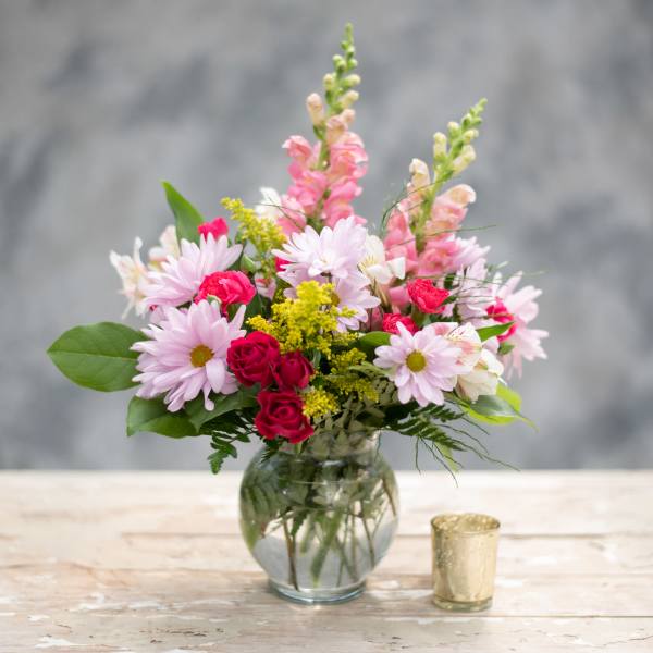 Pink and white mixed bouquet in a glass vase with a small candle holder beside it