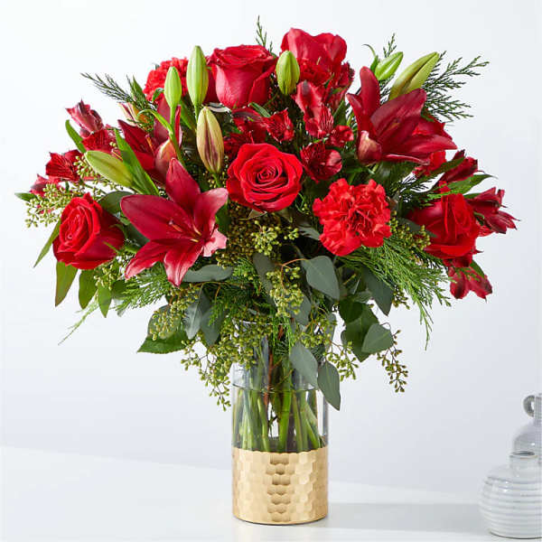 Red roses and lilies in a clear glass vase with a gold wrap