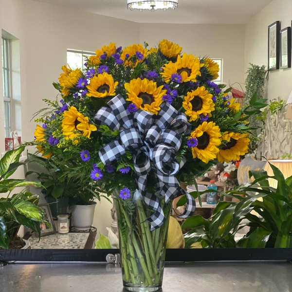 Sunflower bouquet with purple daisies in a clear glass vase and plaid ribbon