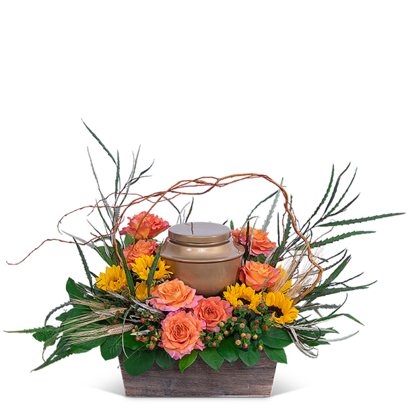 Orange roses and yellow flowers arranged around a bronze urn in a wooden container