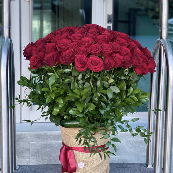 Large bouquet of red roses in a burlap-wrapped container with a pink ribbon
