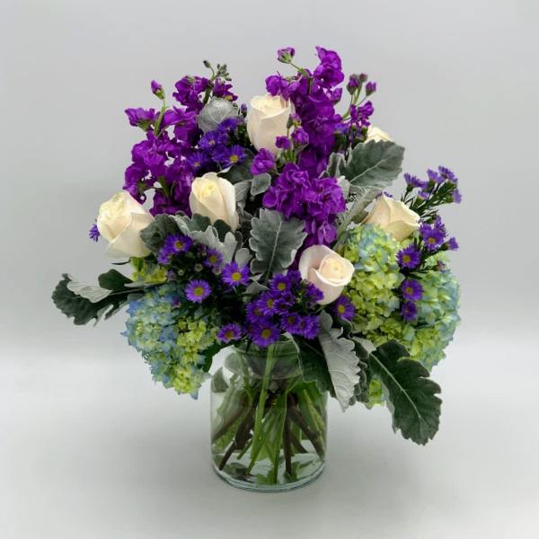 Purple and white flowers arranged in a clear glass vase