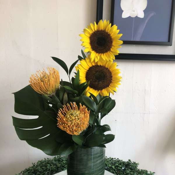 Sunflowers and orange pincushion protea in a tall green vase