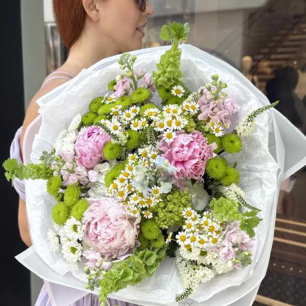 Large bouquet of pink and white flowers with bright green accents wrapped in white paper