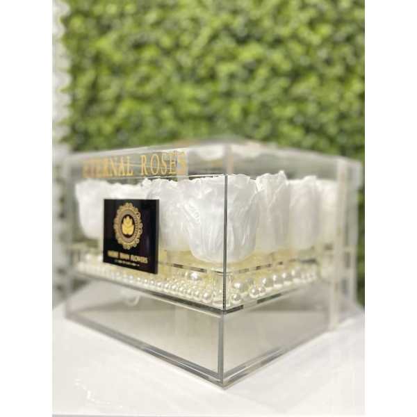 Clear acrylic box filled with white preserved roses arranged above a layer of pearls.