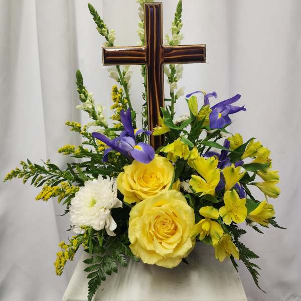 Yellow roses and purple flowers arranged around a wooden cross