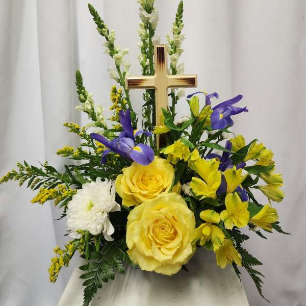 Yellow roses and purple flowers arranged around a gold cross
