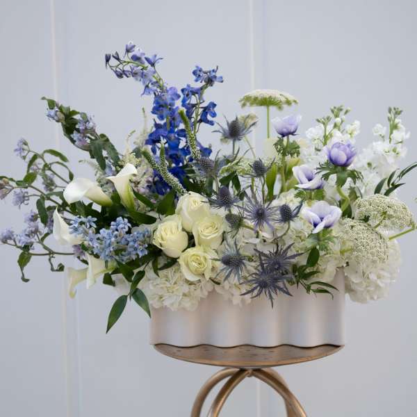 Blue, white, and cream floral arrangement in a white container