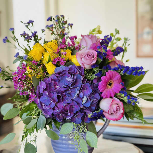Colorful bouquet with purple hydrangea, pink roses, yellow roses, and a pink gerbera daisy in a vase